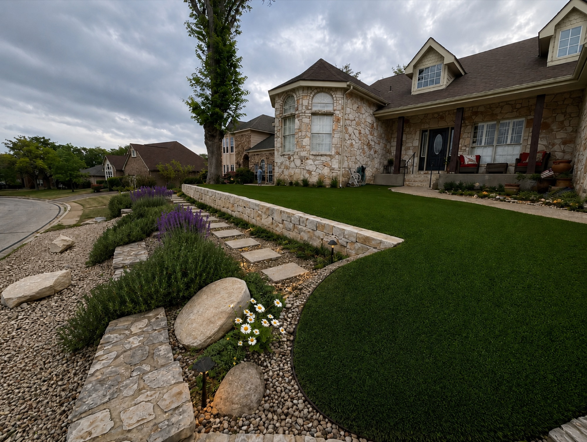 Finer landscape designs — limestone-veneer home with curved artificial turf, dry-stack retaining wall, lavender and rosemary plantings, flagstone path, river-stone borders, low-voltage path lighting