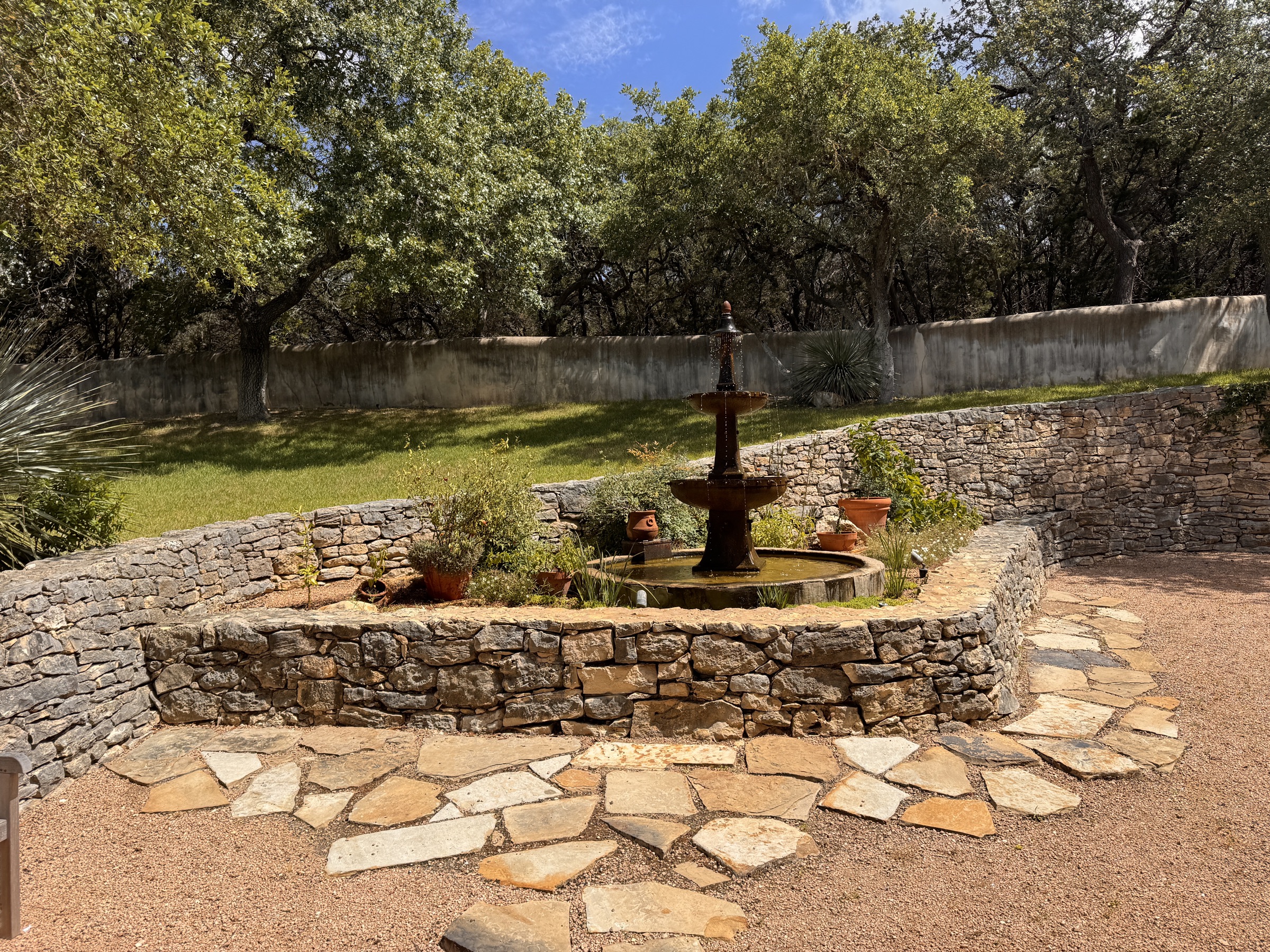 Patio, dry-stack limestone wall, tiered bronze fountain and flagstone hardscape under Hill Country oak canopy